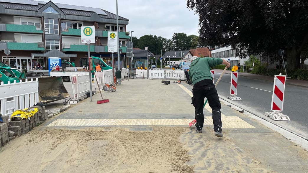 Ein Arbeiter in grüner Kleidung verstreicht Sand auf einer neu verlegten Pflasterstraße