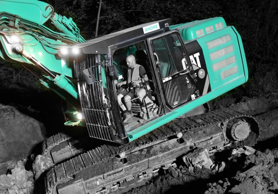 Bauarbeiter bedient einen großen grünen Bagger bei Nacht, mit beleuchteten Scheinwerfern