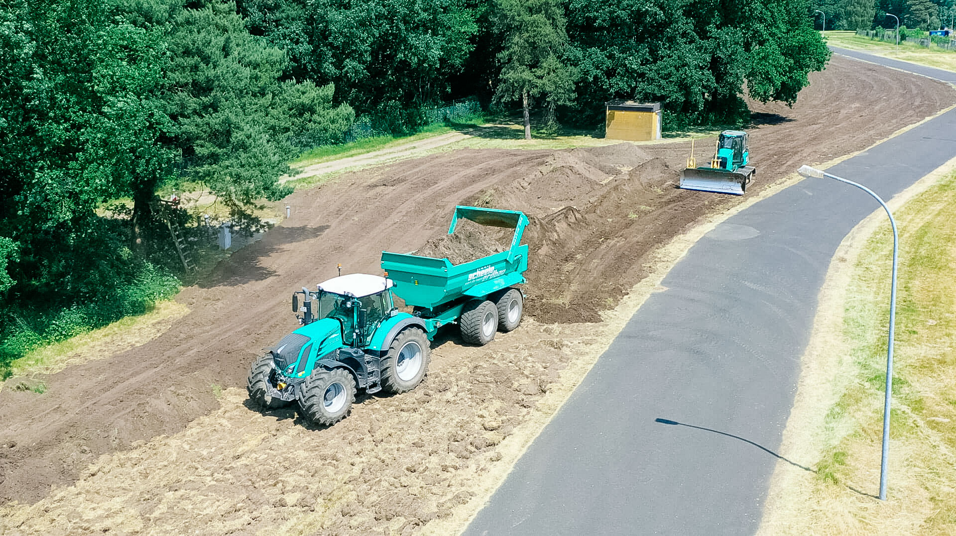 Luftaufnahme der Baustelle mit grünem Muldenkipper, modernem Traktor und kleinem Baufahrzeug.