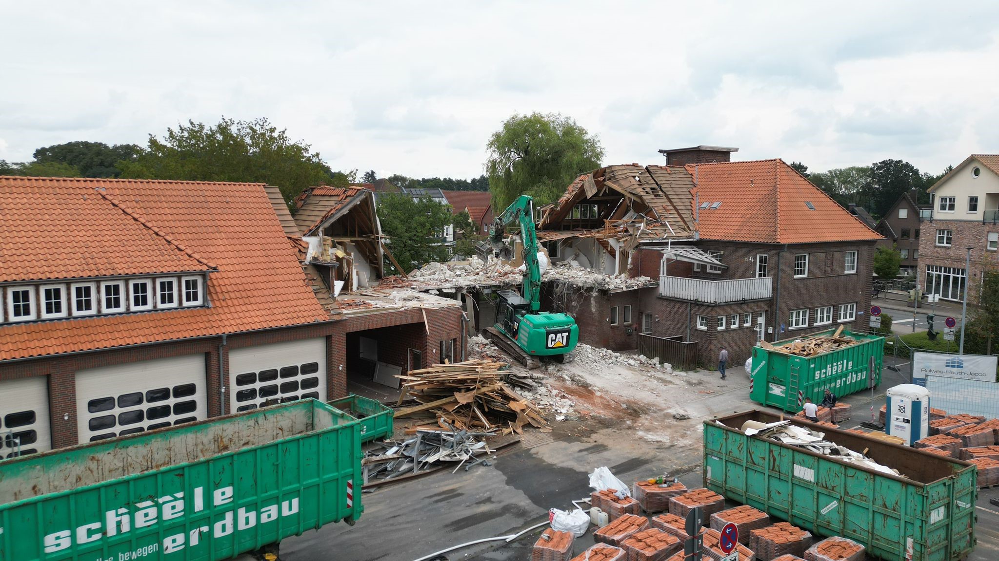 Abrissarbeiten in städtischem Gebiet mit Bagger, zerstörtem Ziegelgebäude und Containern